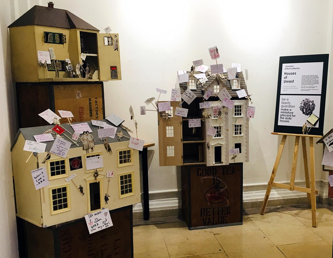 Houses of unrest - three traditional dolls houses covered in placards created by exhibition visitors