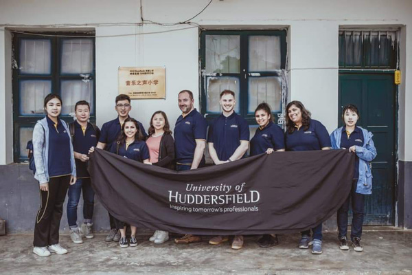 A group photo with people holding a flag with the University of huddersfield logo on it.