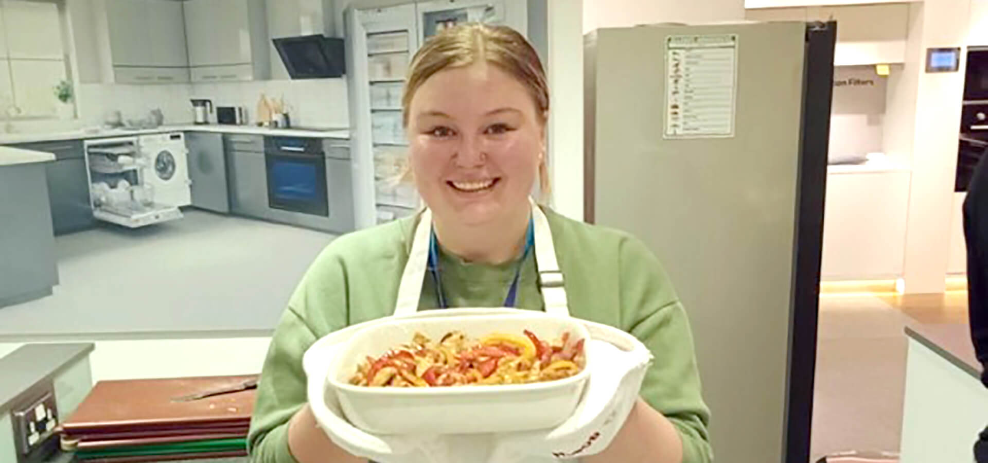 Beth holds up a dish of food in a kitchen while doing some training/team building in a showroom