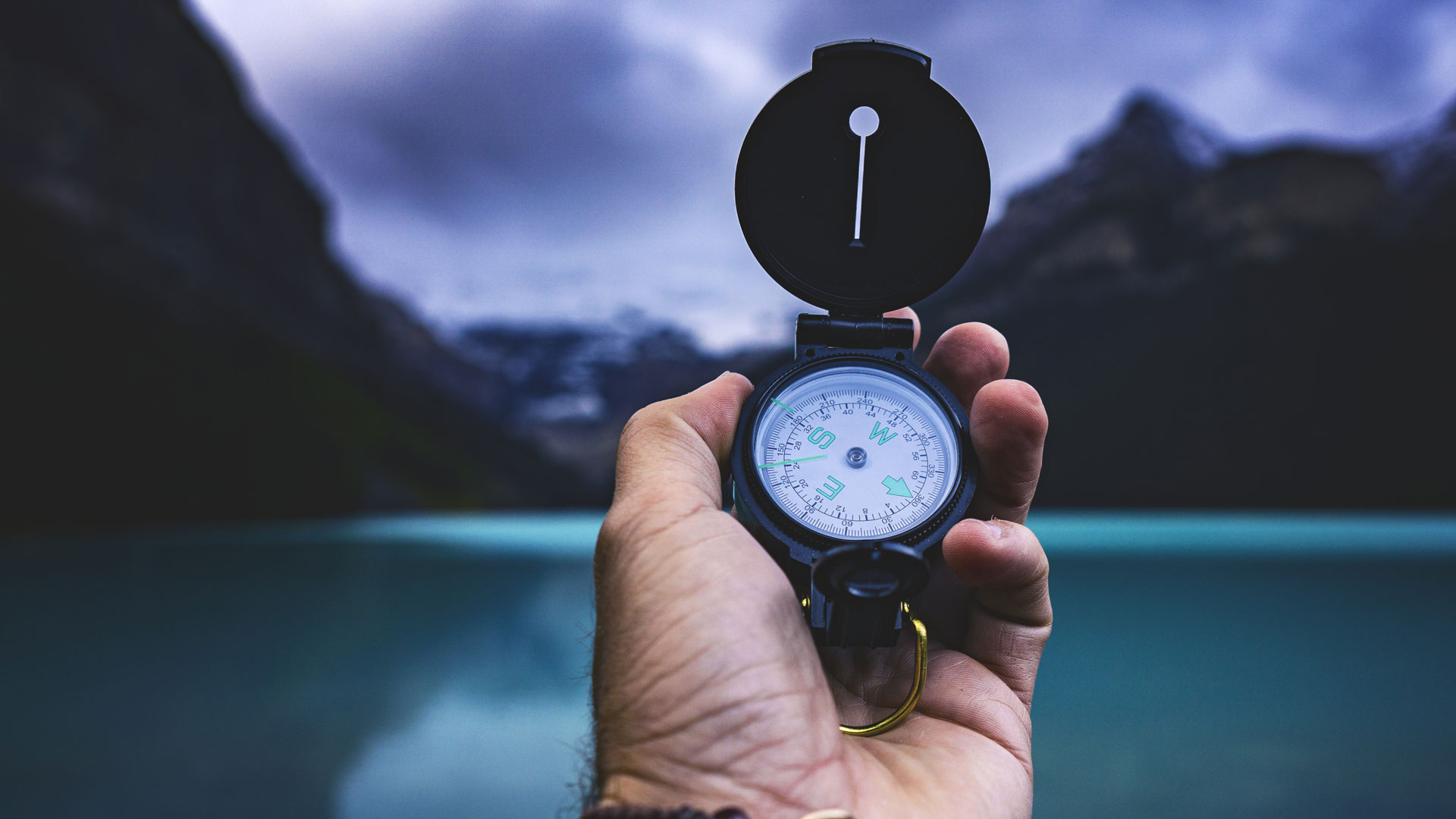 Hand holding compass infront of lake and mountains