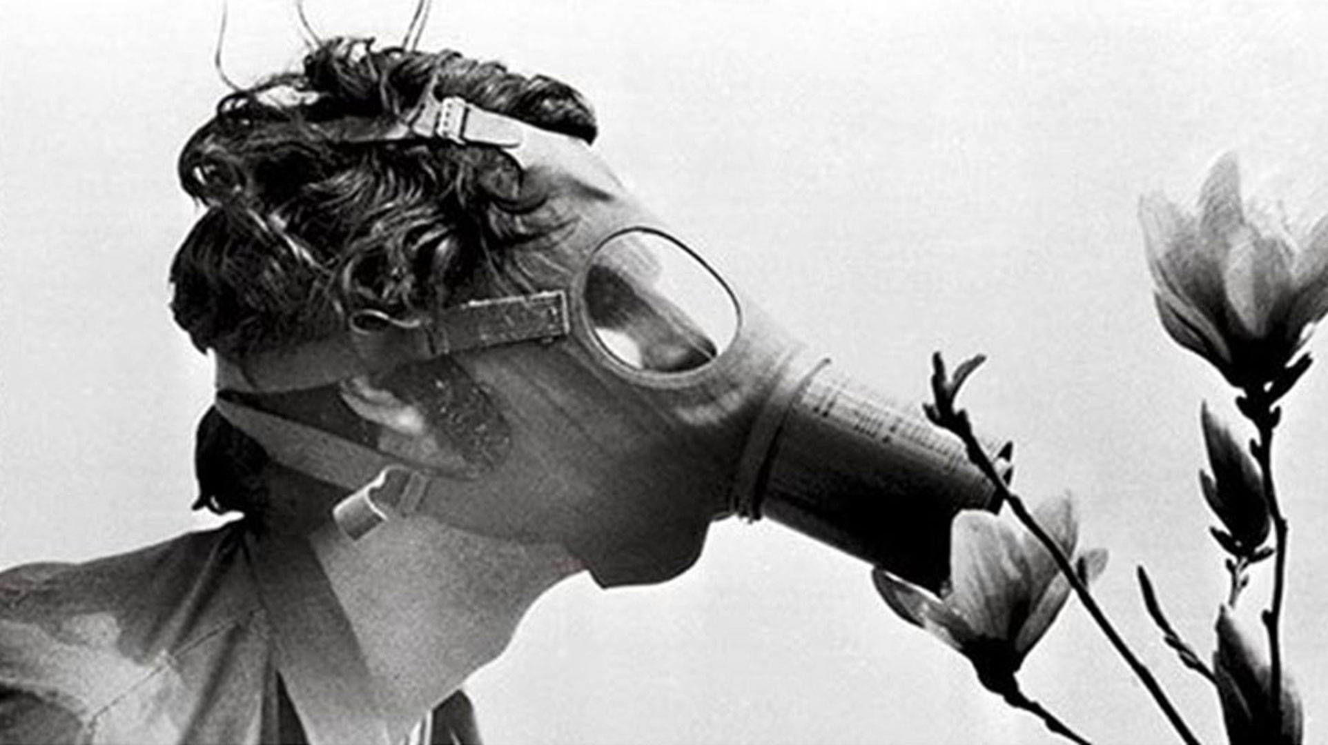 Black and white photo of person in gasmask smelling flowers from Earthday 1970