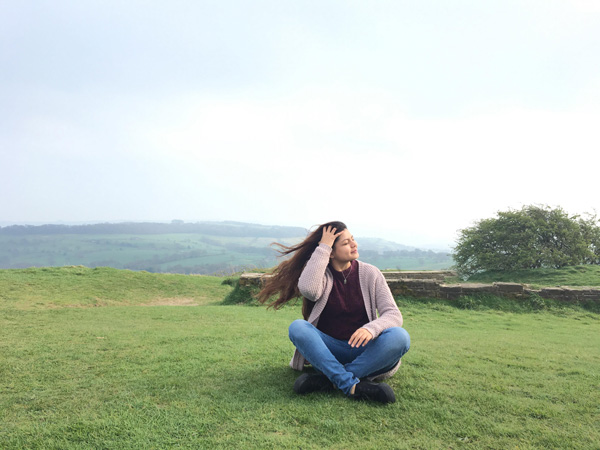 A student sitting in a field with wind blowing through her hair