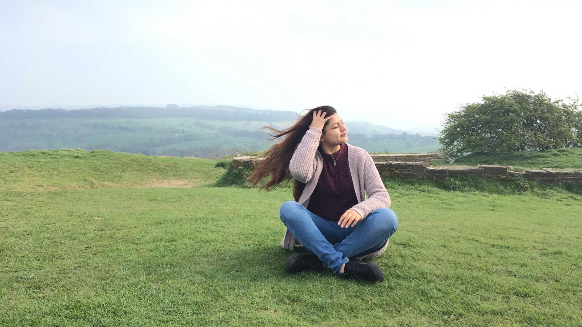 A student sitting in a field with wind blowing through her hair