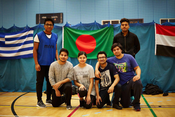 A group of students in a global society smiling and holding a flag in a sports hall