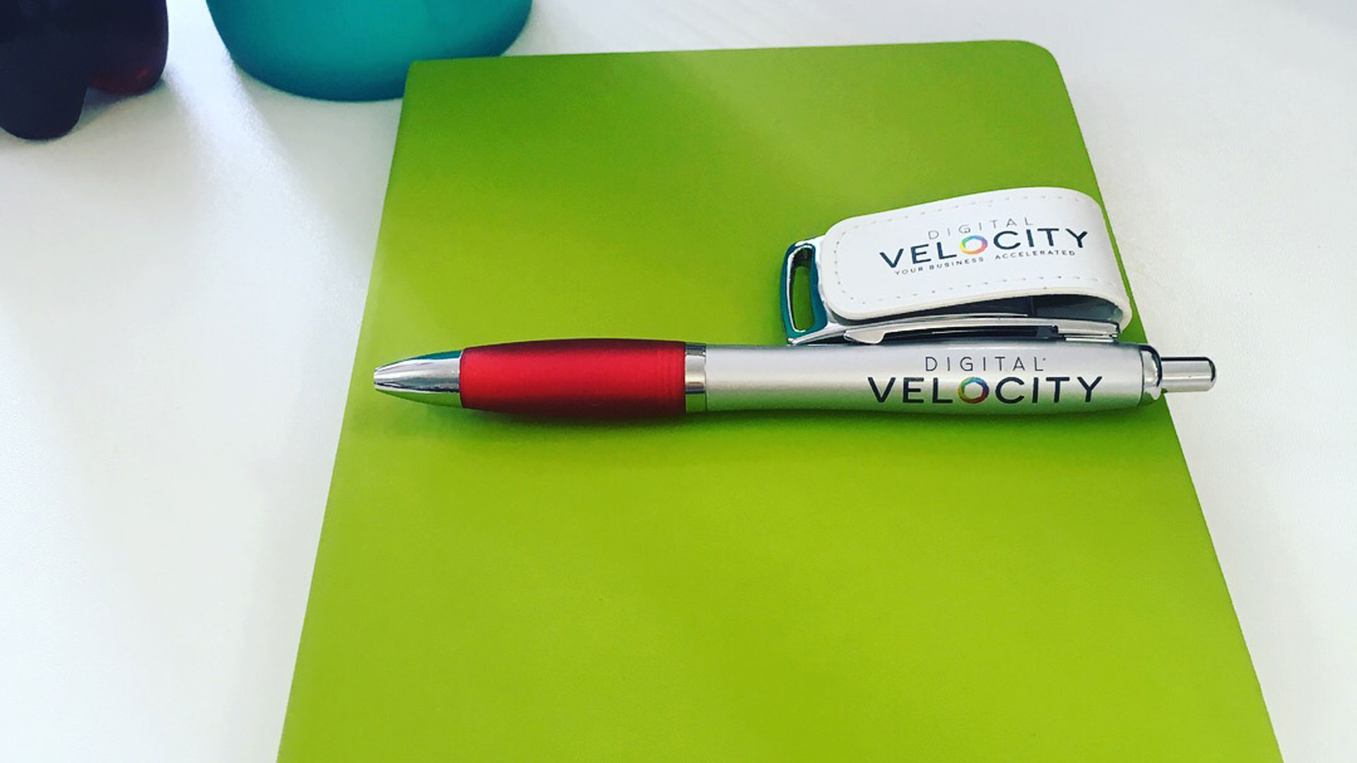 A photo of a notebook with a Digital Velocity branded pen and usb drive.