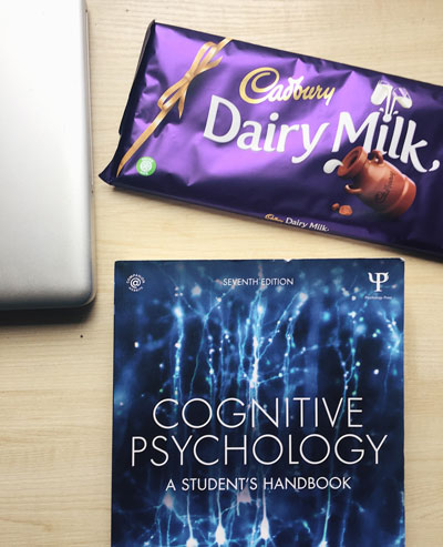 A photo of a table with a laptop, textbook and chocolate on it