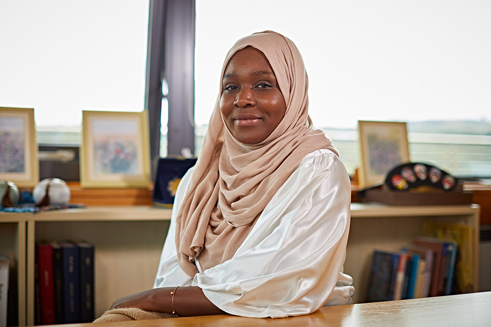 University of Huddersfield alumna, Ruky Yussuf sat at an office desk.