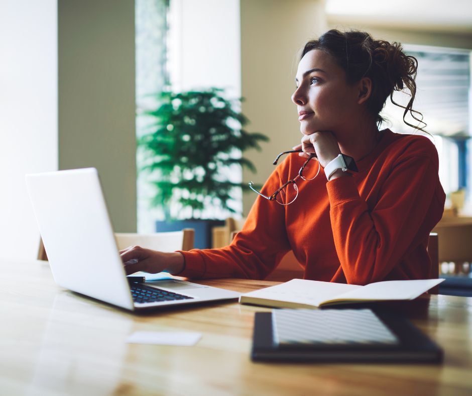 A female student looks into the distance while sitting in front of a laptop computer