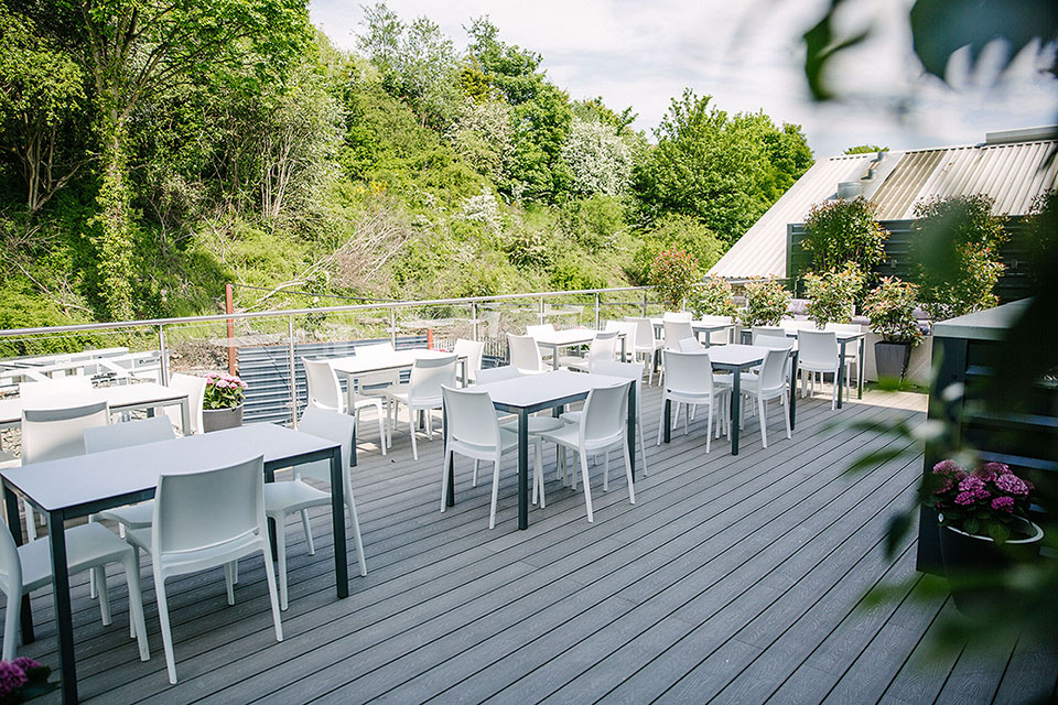 An outdoor deck with lots of tables and chairs set out cabaret style with a lush green forest in the background