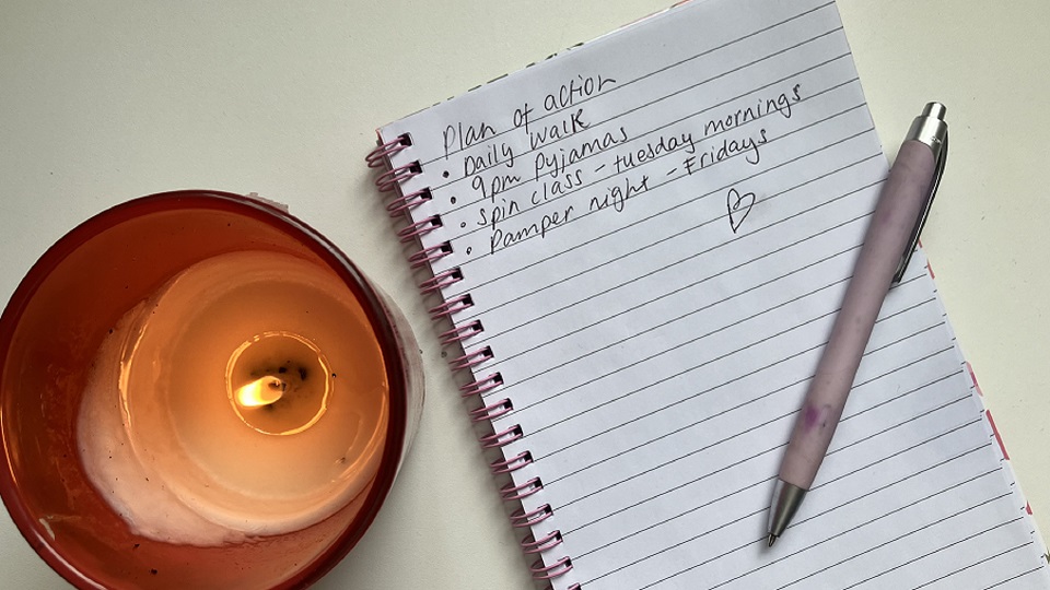 A candle, next to a handwritten list in notebook