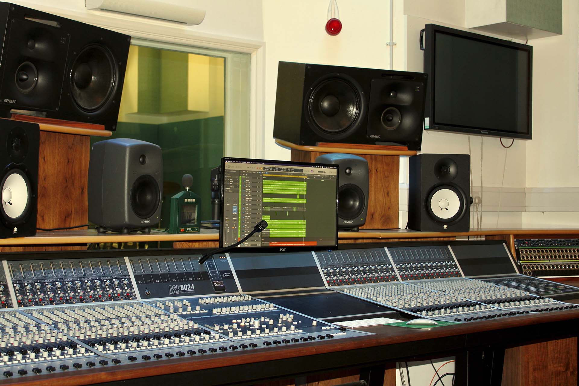 An image of a sound mixing desk surrounded by several speakers and a monitor