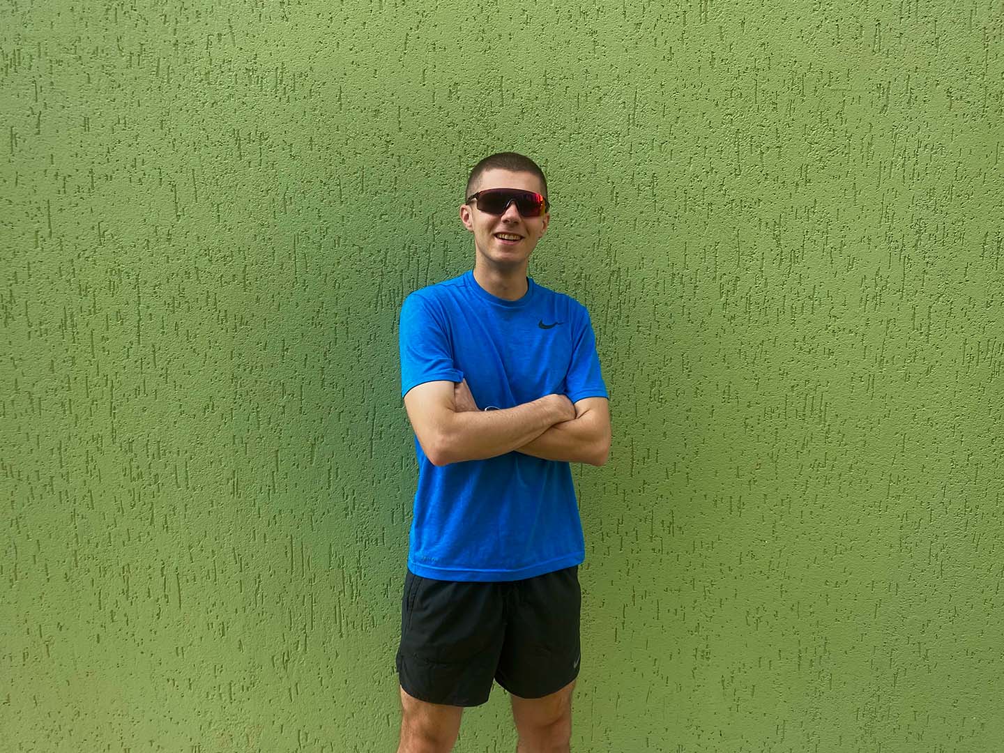 AJ stands in his running kit, a blue tshirt and black shorts, in front of a plain green painted wall