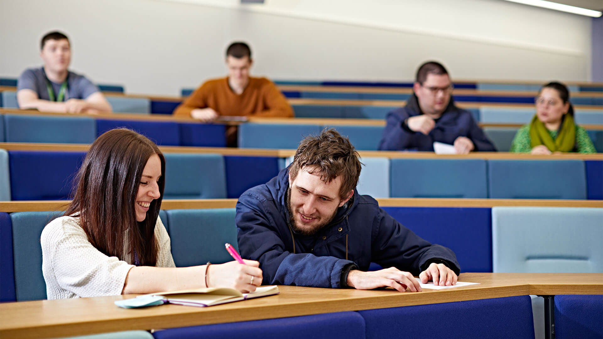 A disability support assistant helping a student take notes in a lecture.