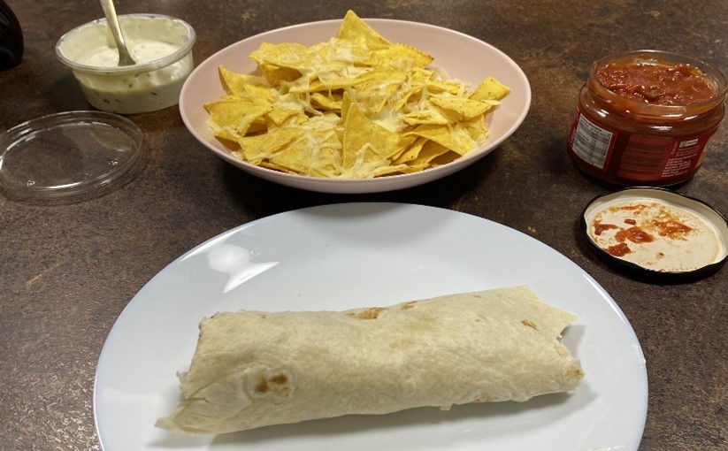 A homemade chicken wrap with a bowl of tortilla chips