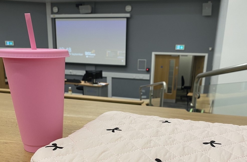 A view towards a screen at the front of a lecture theatre, with a bag and pink reusable drink cup in the foreground