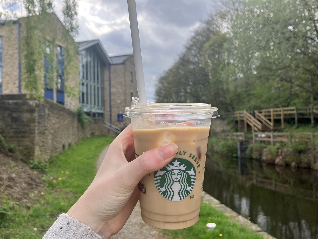 A hand holding an iced coffee in front of a canal