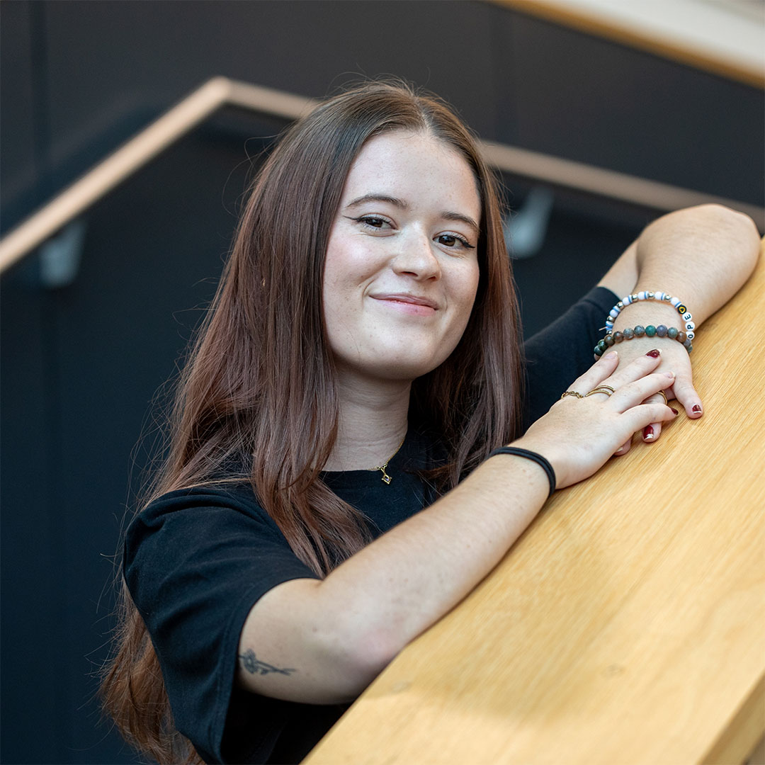 Hope smiling and leaning on a railing in an indoor setting.