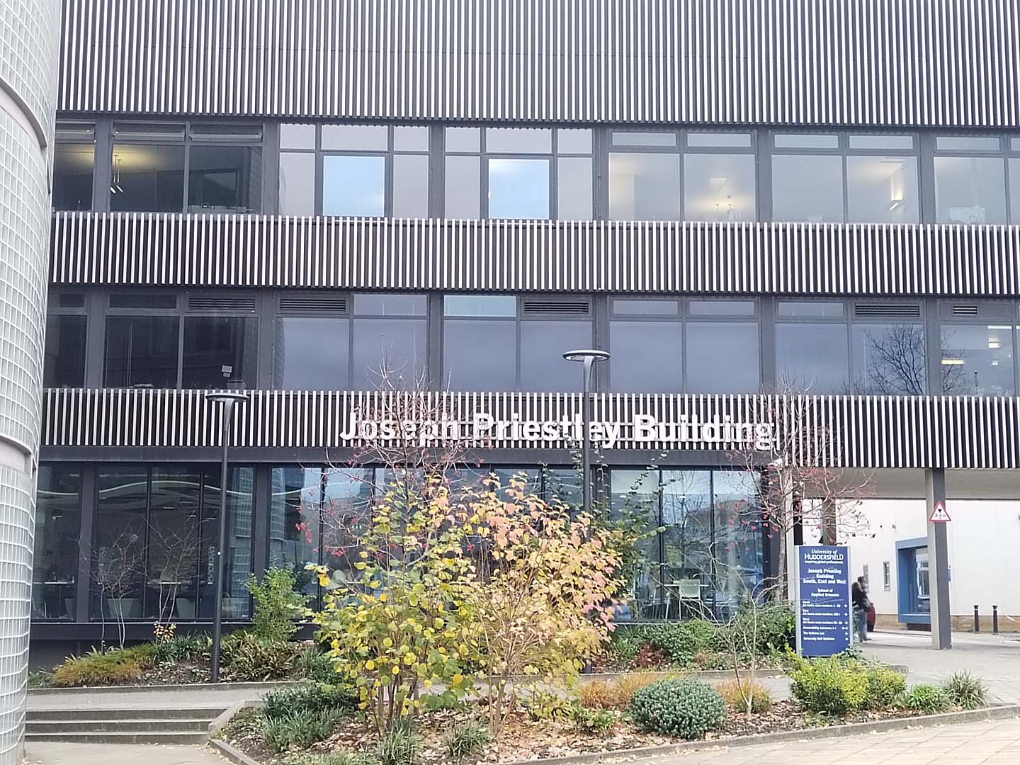 Exterior view of the Joseph Priestley Building at a university campus, featuring modern architecture with horizontal black and white striped detailing.