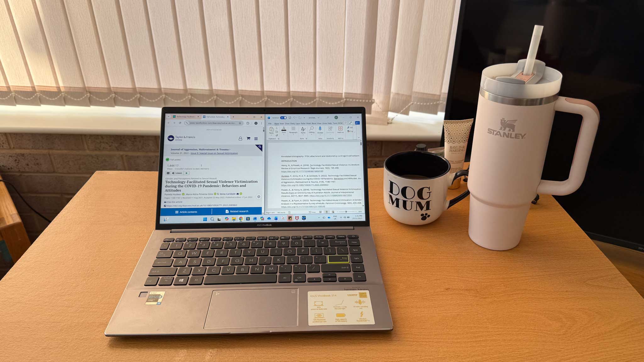 A laptop on a desk with water bottle and mug next to it
