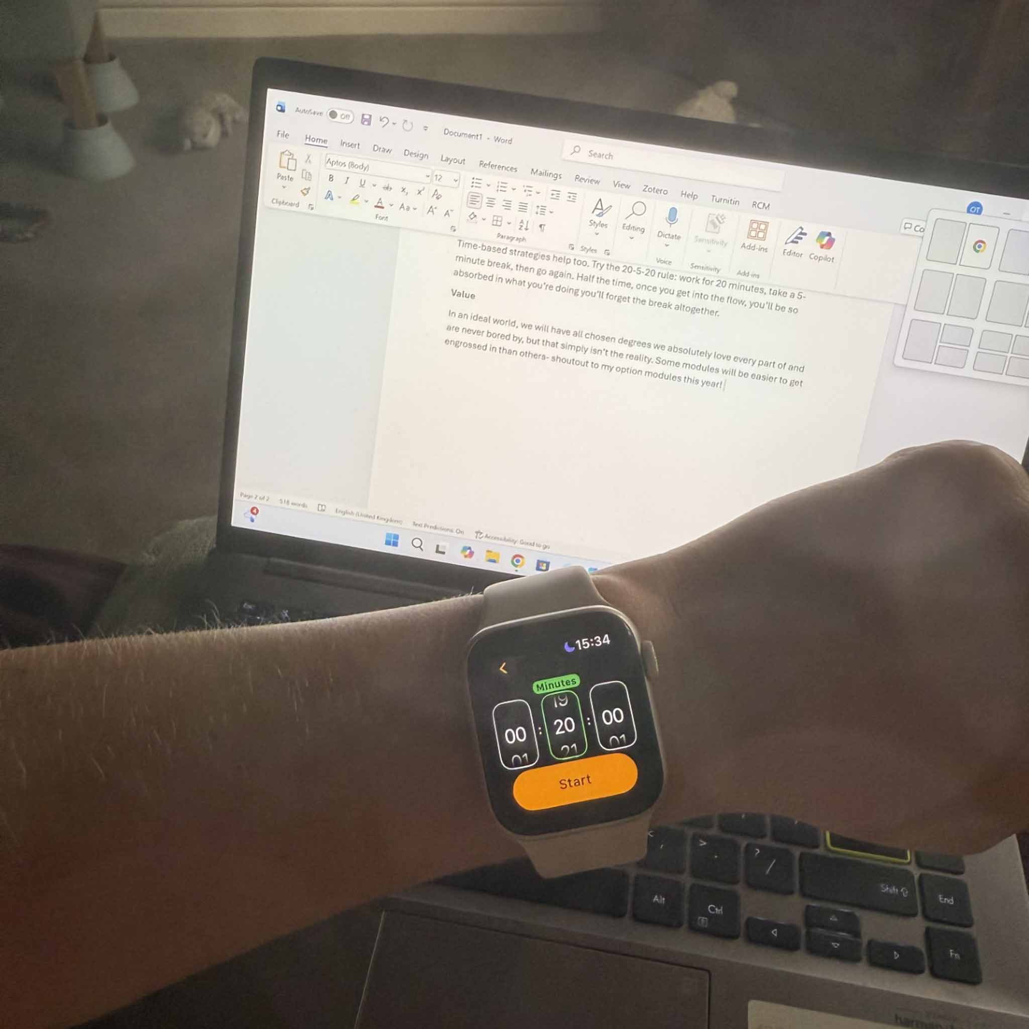 An arm with a watch above a laptop