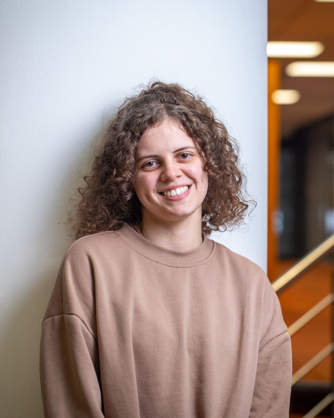 A student leaning against a wall smiling