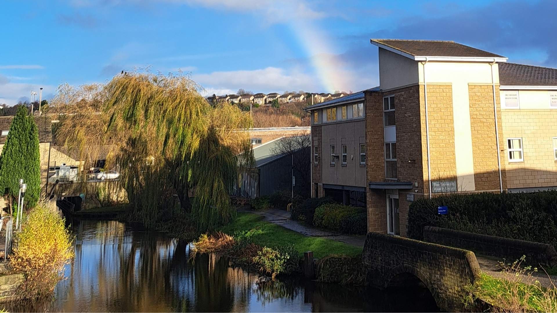 A pale brick building next to a canal, with a rainbow in the sky
