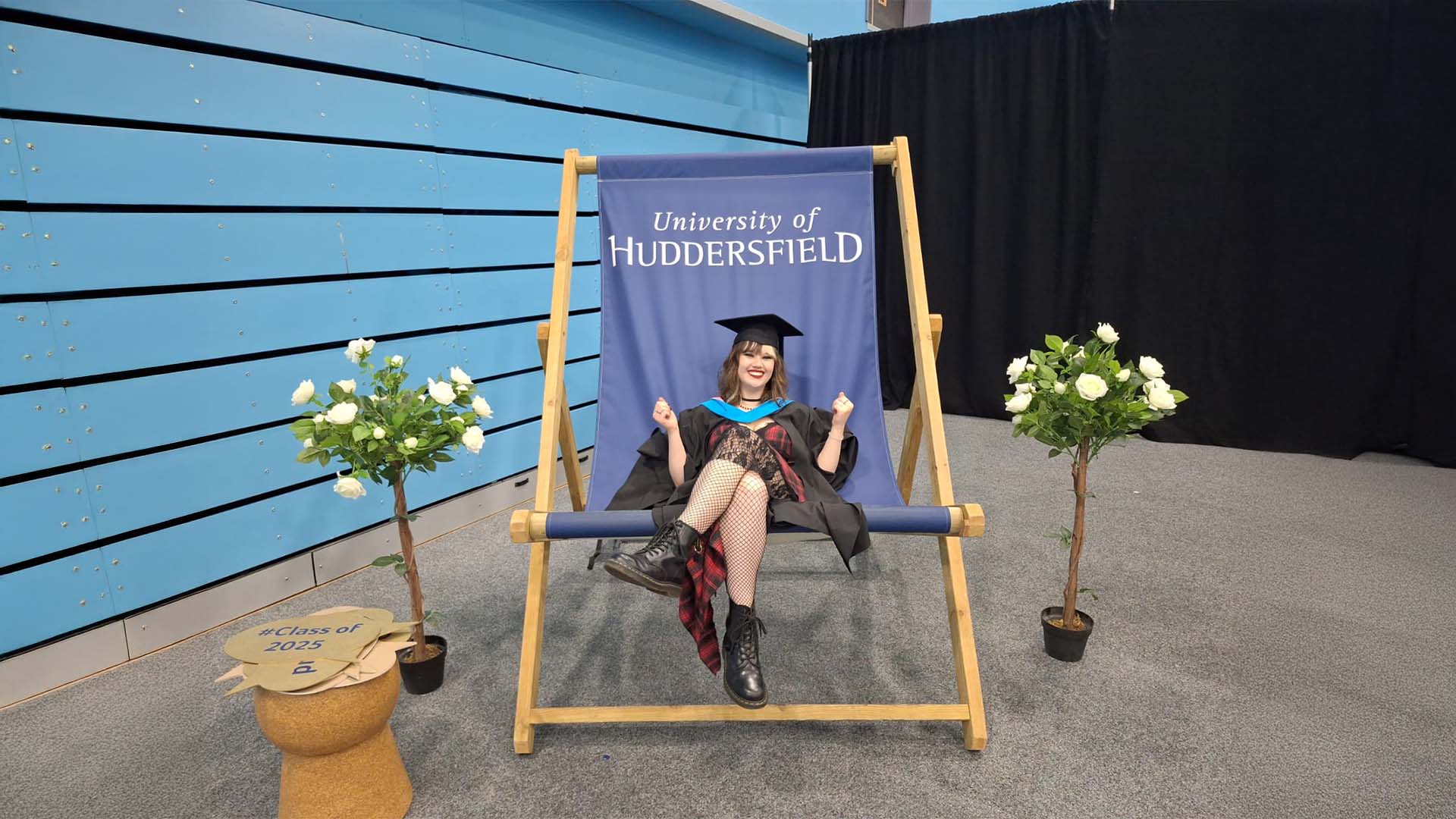 Maisy in academic regalia sits on a large deck chair labeled 