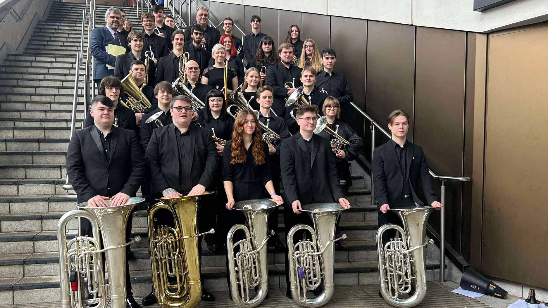 Group photo of a brass band with various instruments, including trombones and tubas, posed on stairs.