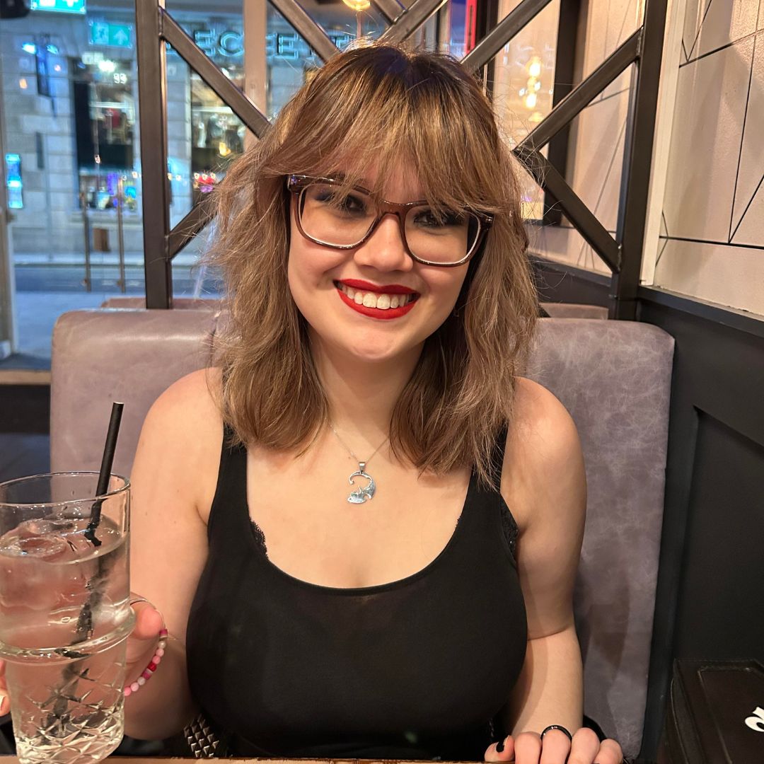 A smiling student sitting down holding a drink and smiling