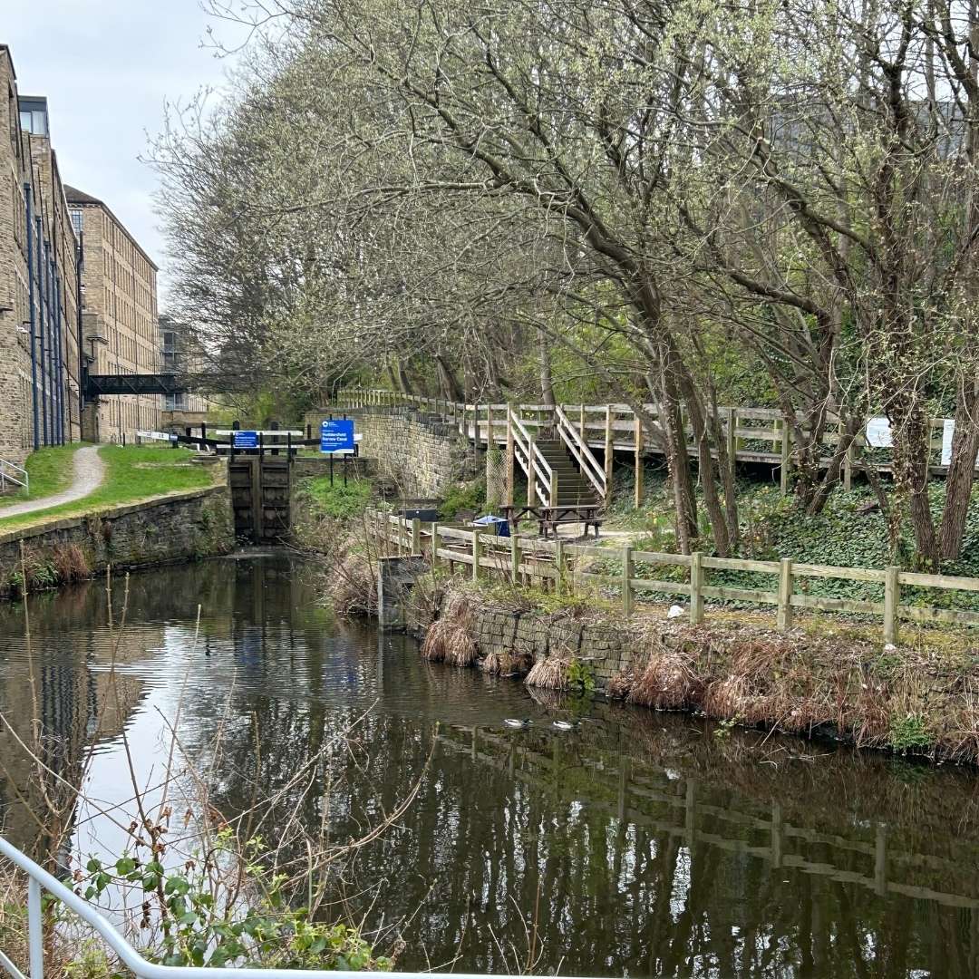 a canal surrounded by woodland on one side and mill buildings on the other