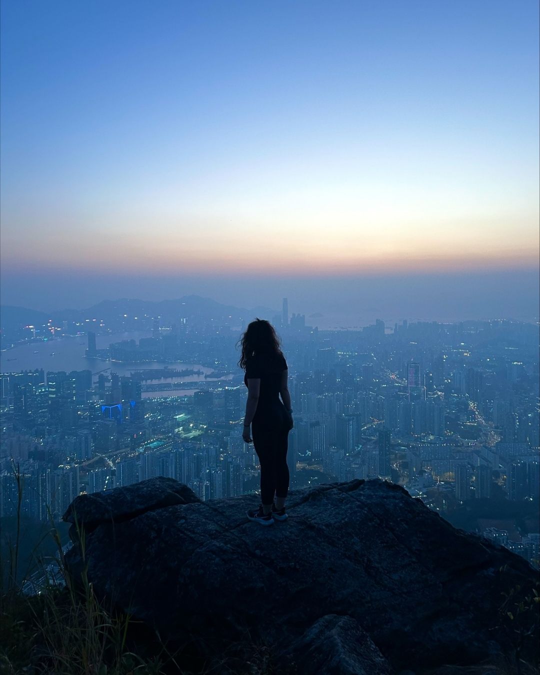 A silhouette of a person on a mountain top overlooking a city