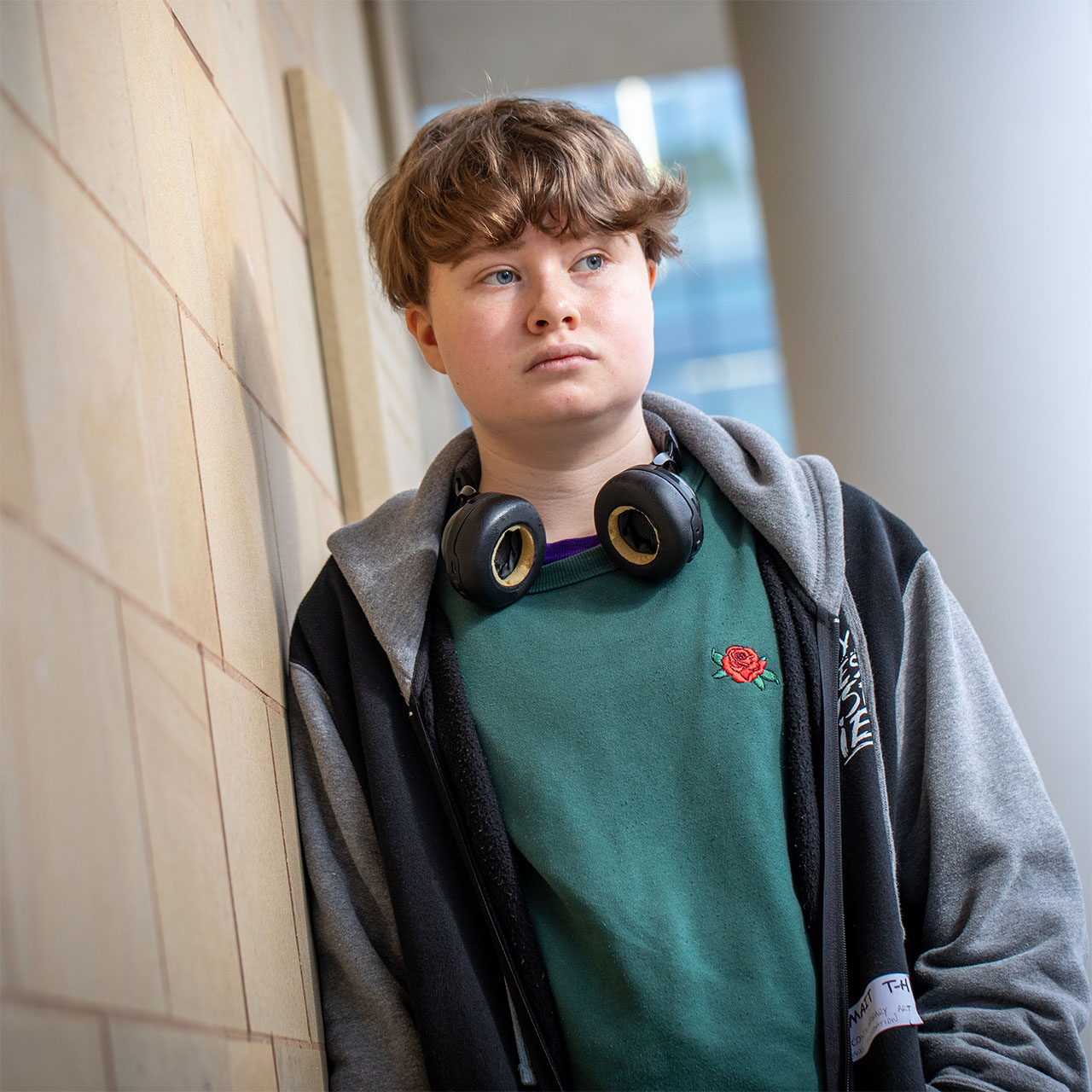 Person with headphones around their neck, wearing a dark jacket over a green T-shirt, standing outside the Steinitz building.