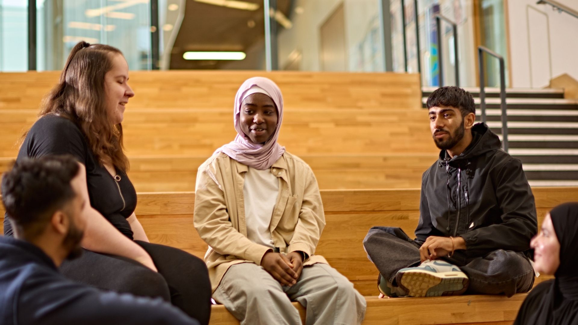 Five students sit talking on a wooden tiered seating area