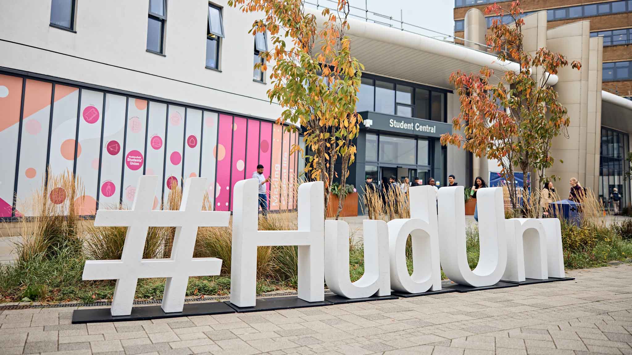 Large letters spell out #HudUni outside a modern white building
