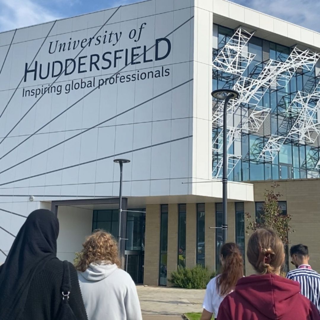 Students walking towards a white building which says University of Huddersfield on the side