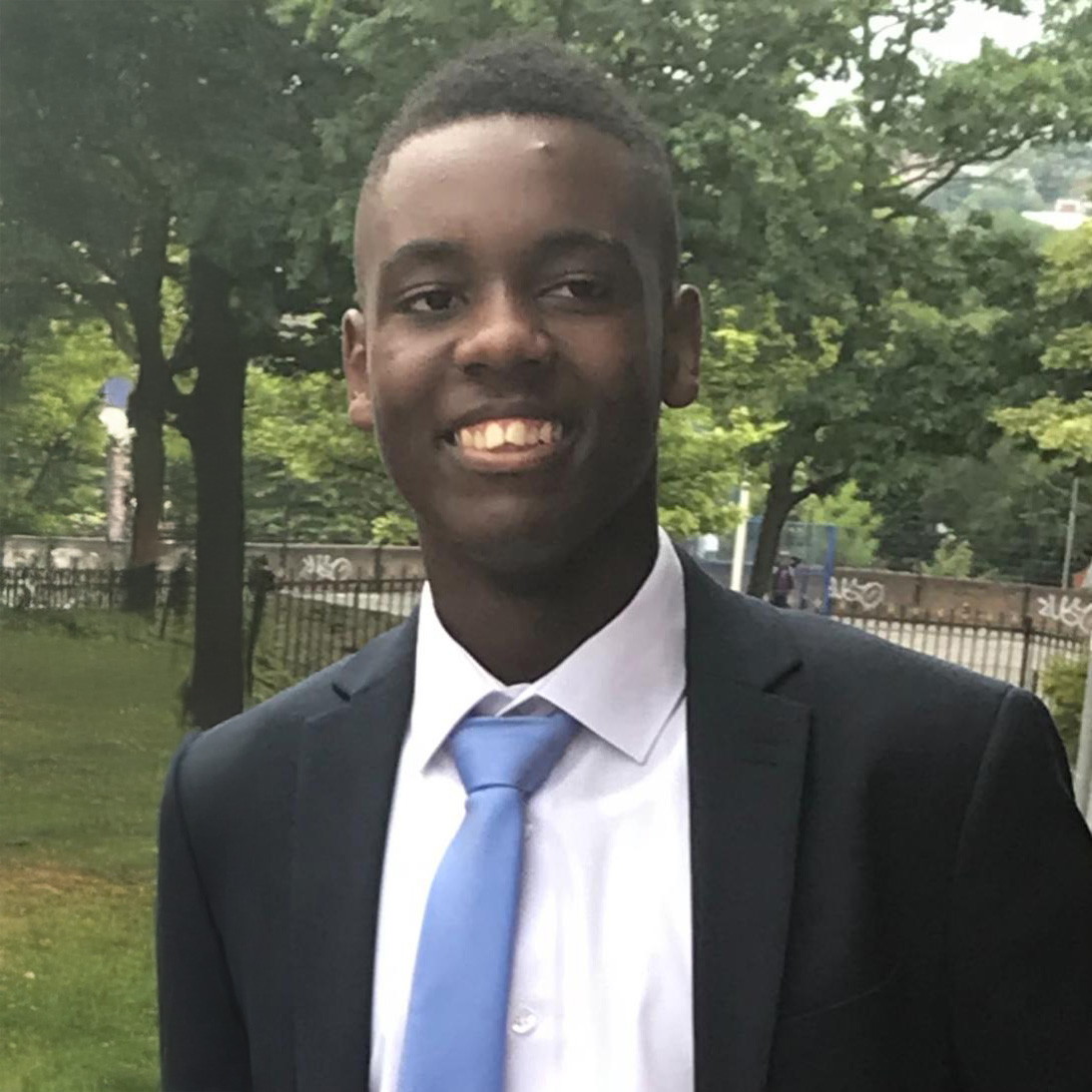 Moses Colley. Person in a business suit smiling in a park setting.