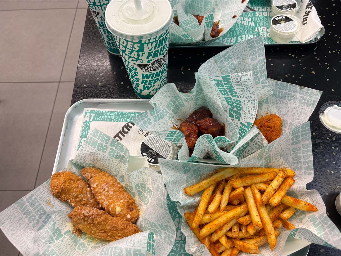 A tray of Wingstop food, featuring breaded chicken wings and seasoned fries, served alongside branded paper cups.