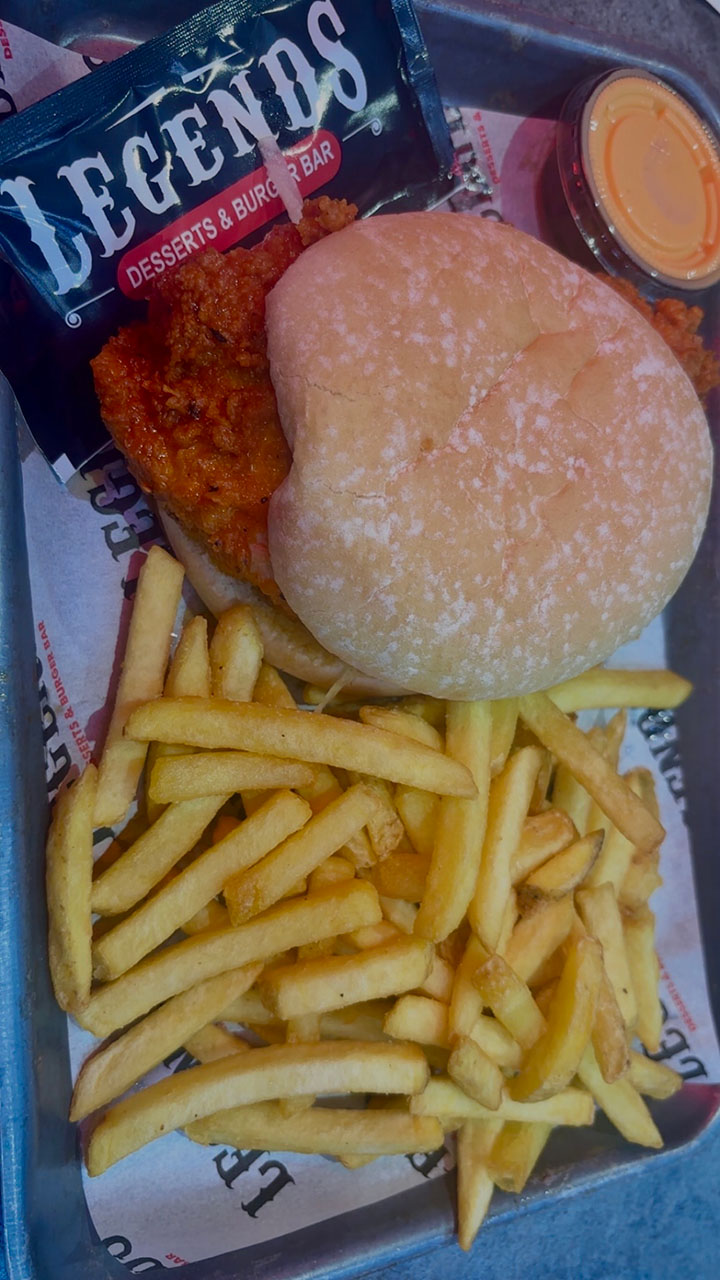 Plate of food from Legends Desserts & Bar, featuring a burger with spicy chicken, a side of fries, and a dipping sauce.