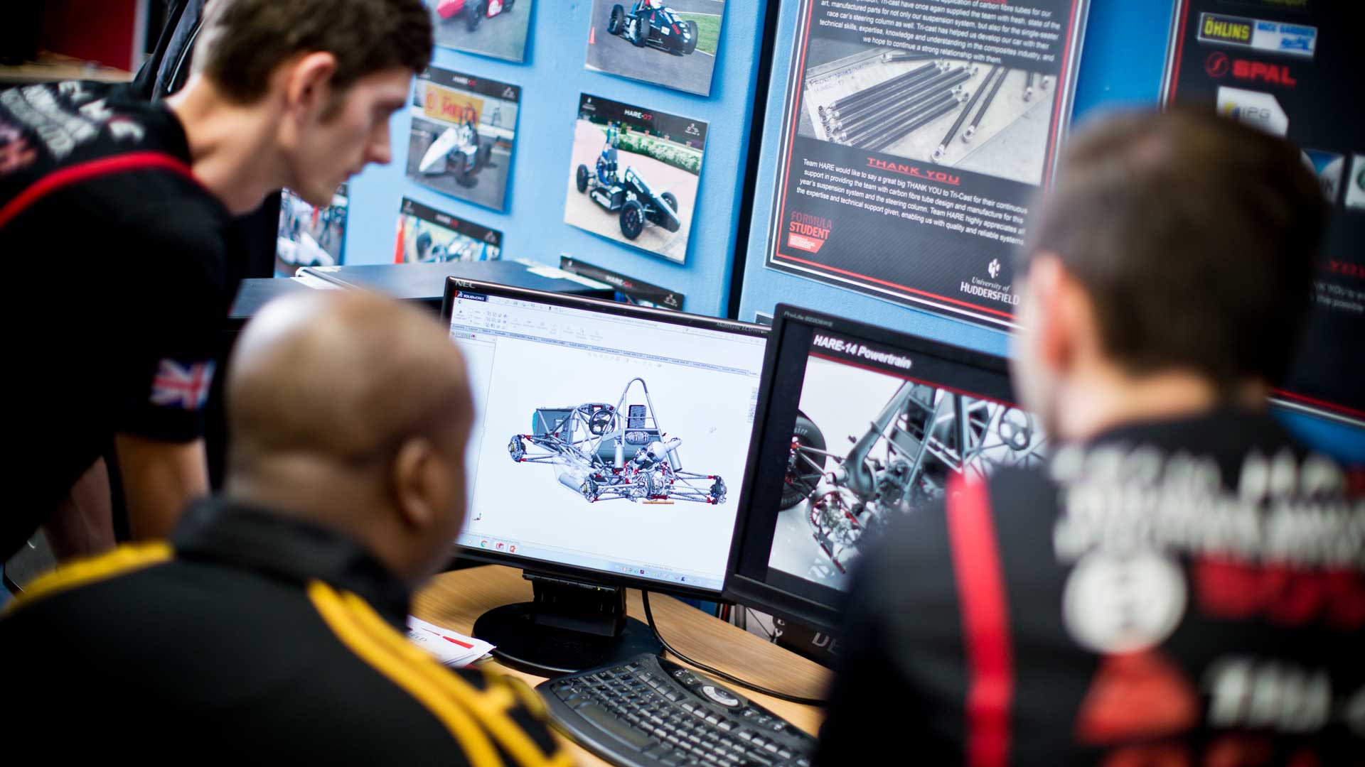 3 members of Team Hare gather around a computer screen to look at a 3D model of a racing car design.