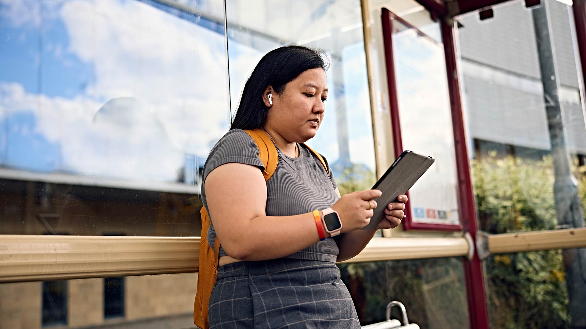 A student stood at a bus stop, looking at their tablet.