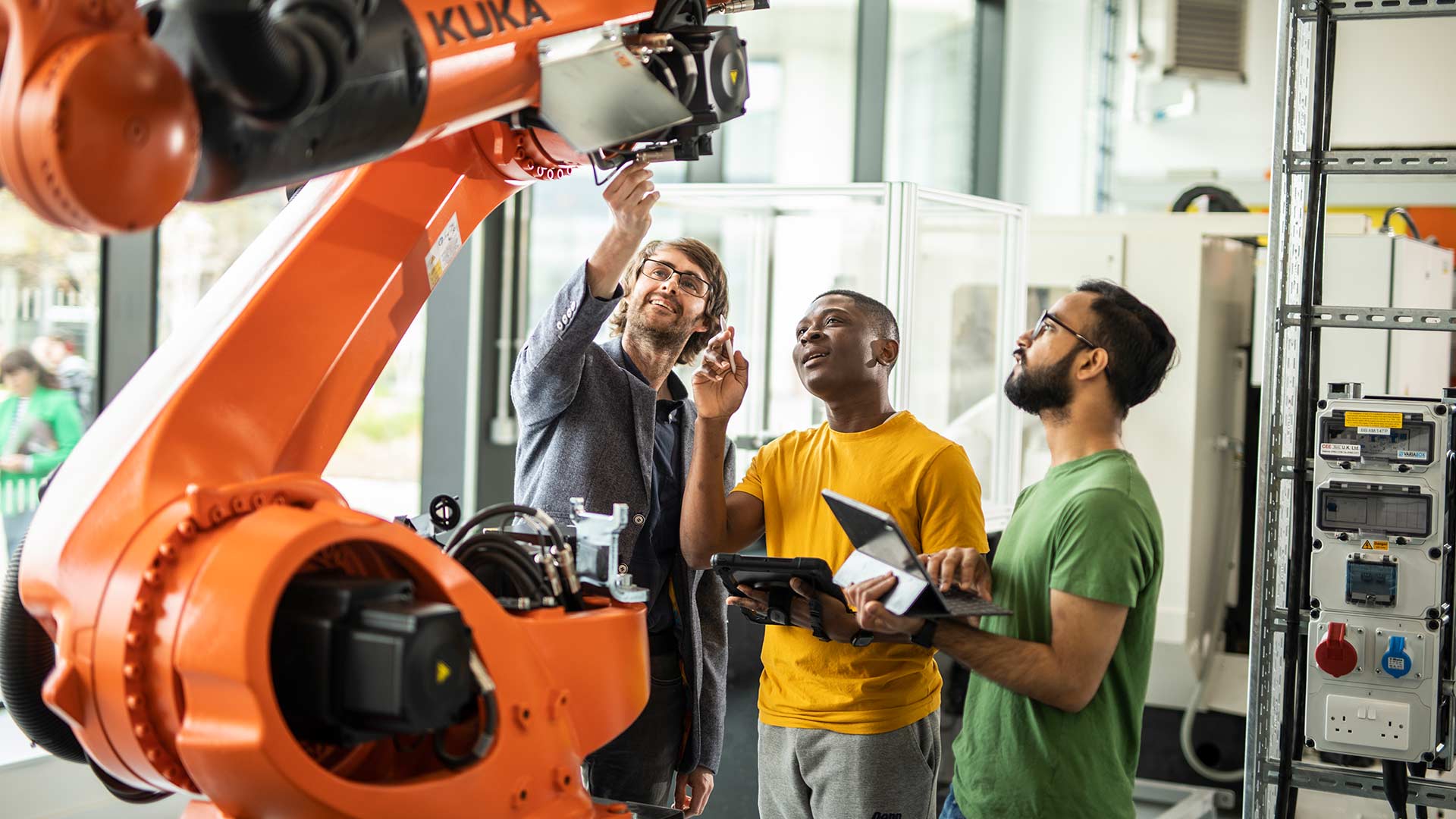 An academic and two students looking up at a piece of engineering equipment.