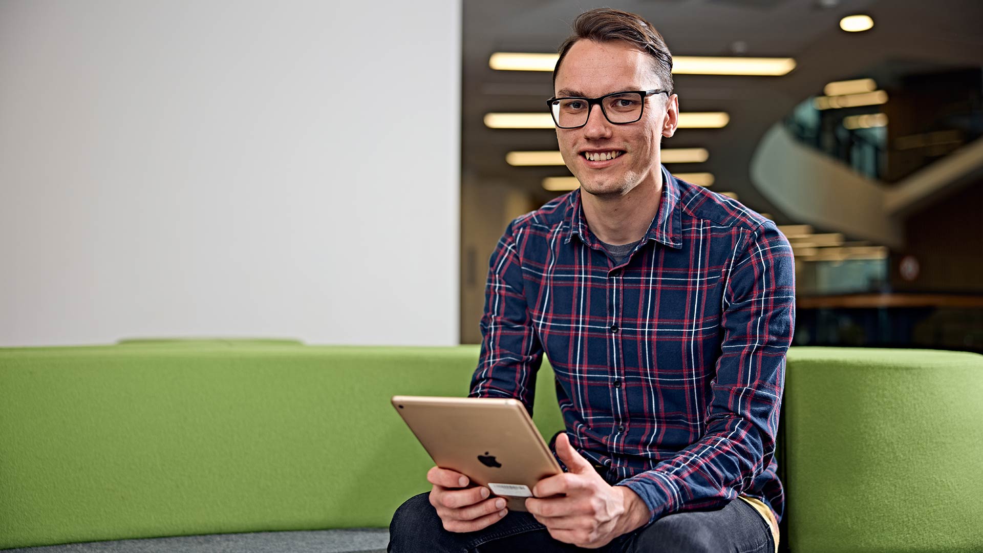 An adult in a shirt, sat down, holding a tablet device.