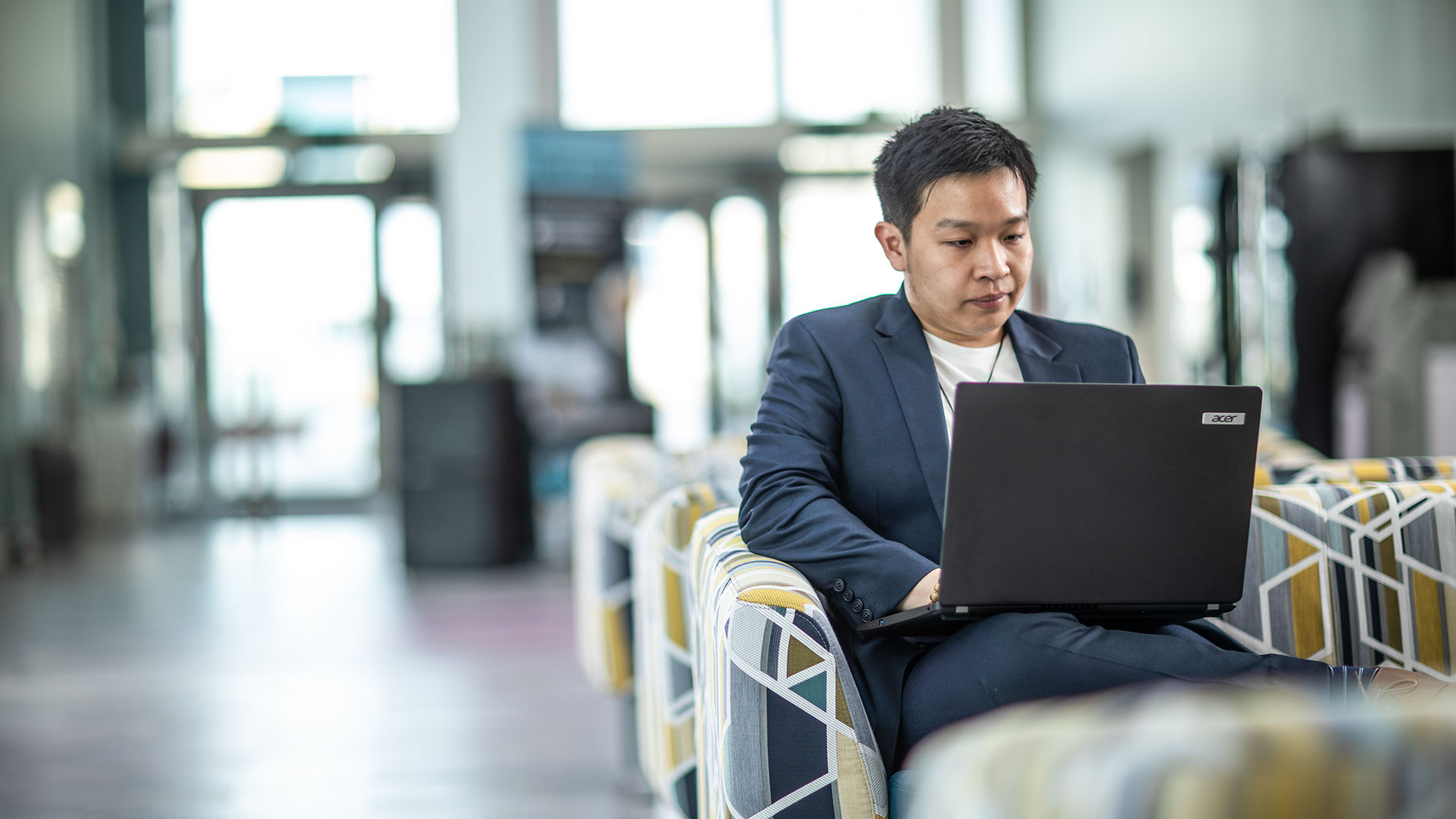 A student in a blazer, working on a laptop in a communal space.