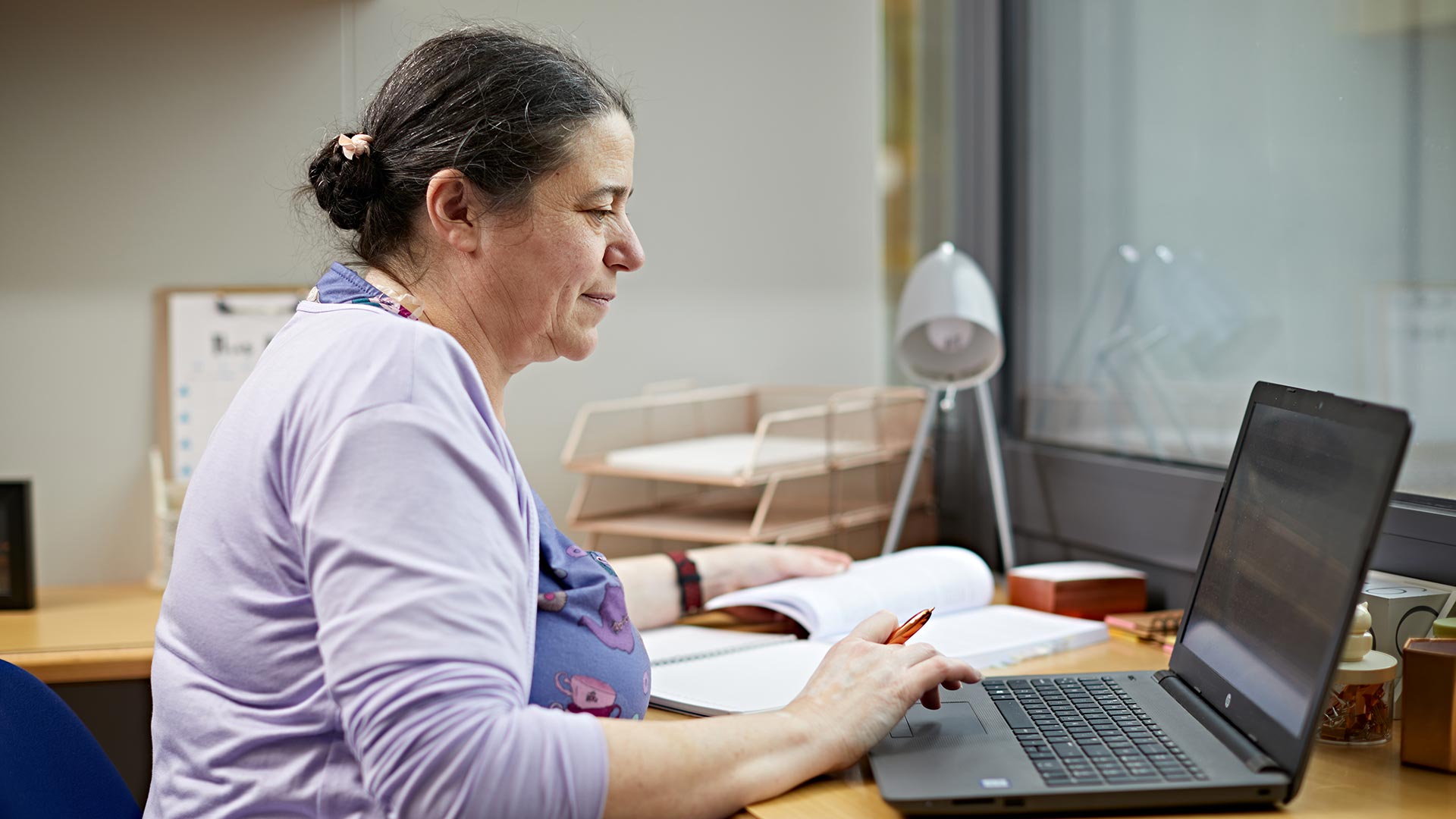 A student working on a laptop at their bedroom desk.