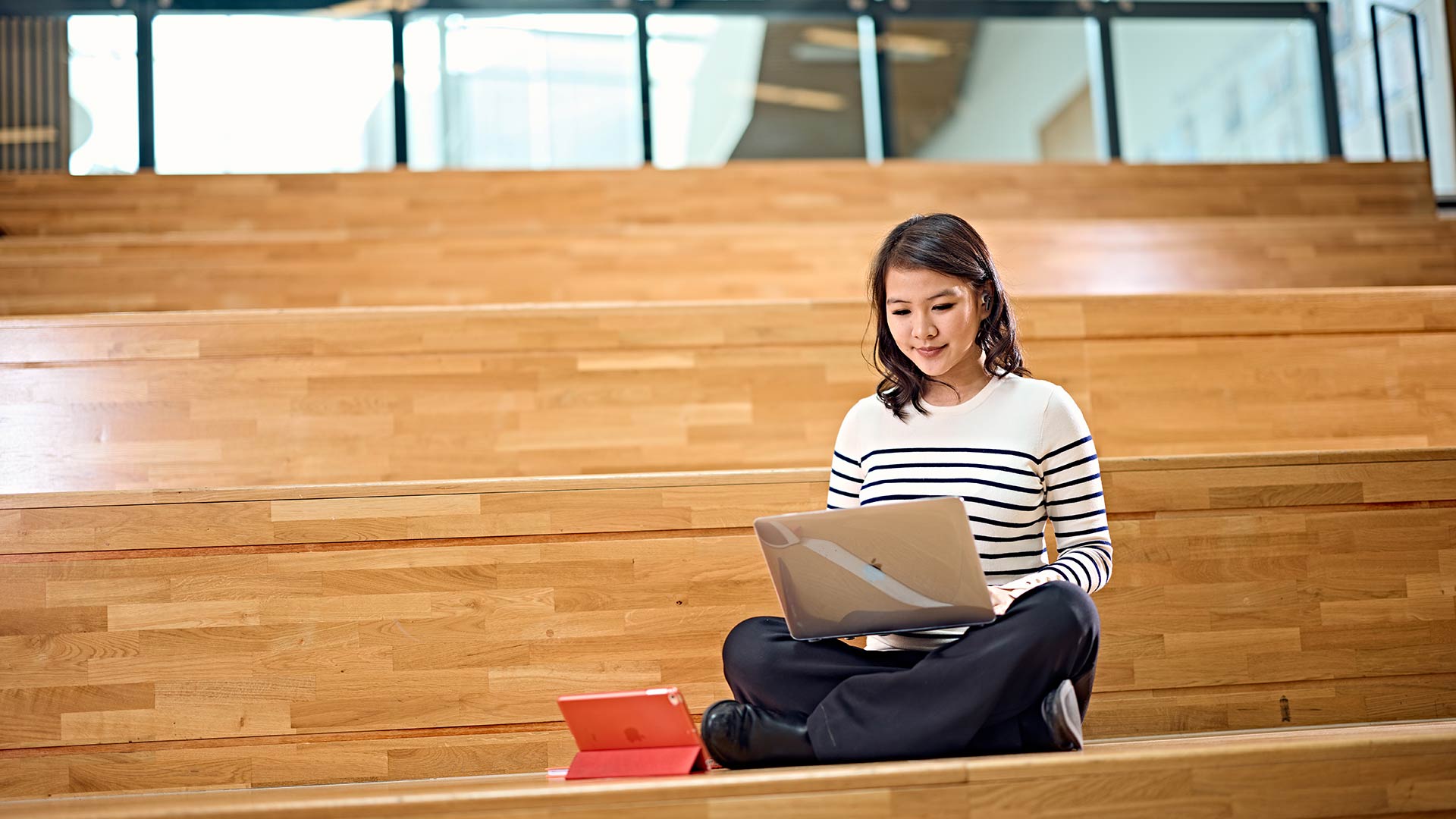 A student sat on some large wooden steps on a laptop.