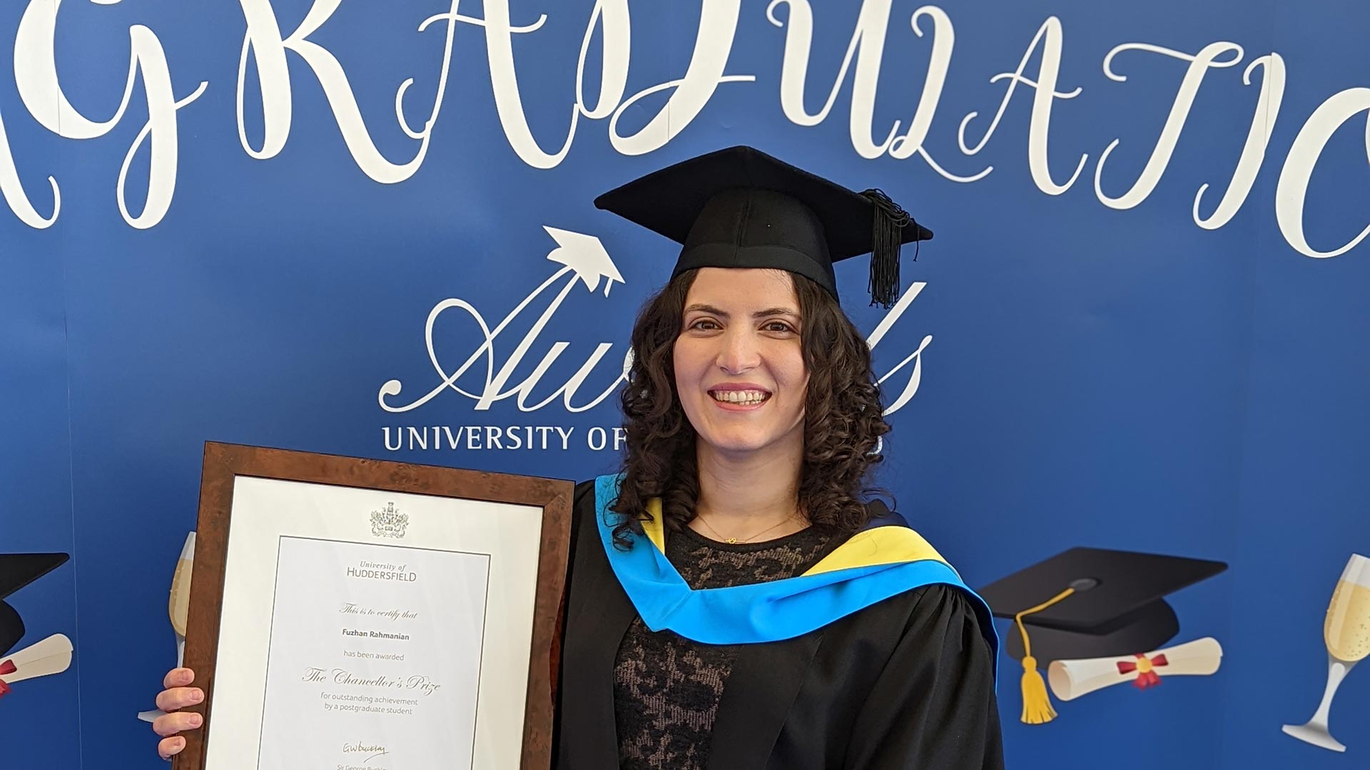 Fuzhan wearing her graduation gown and hat, holding her Chancellors Prize certificate.