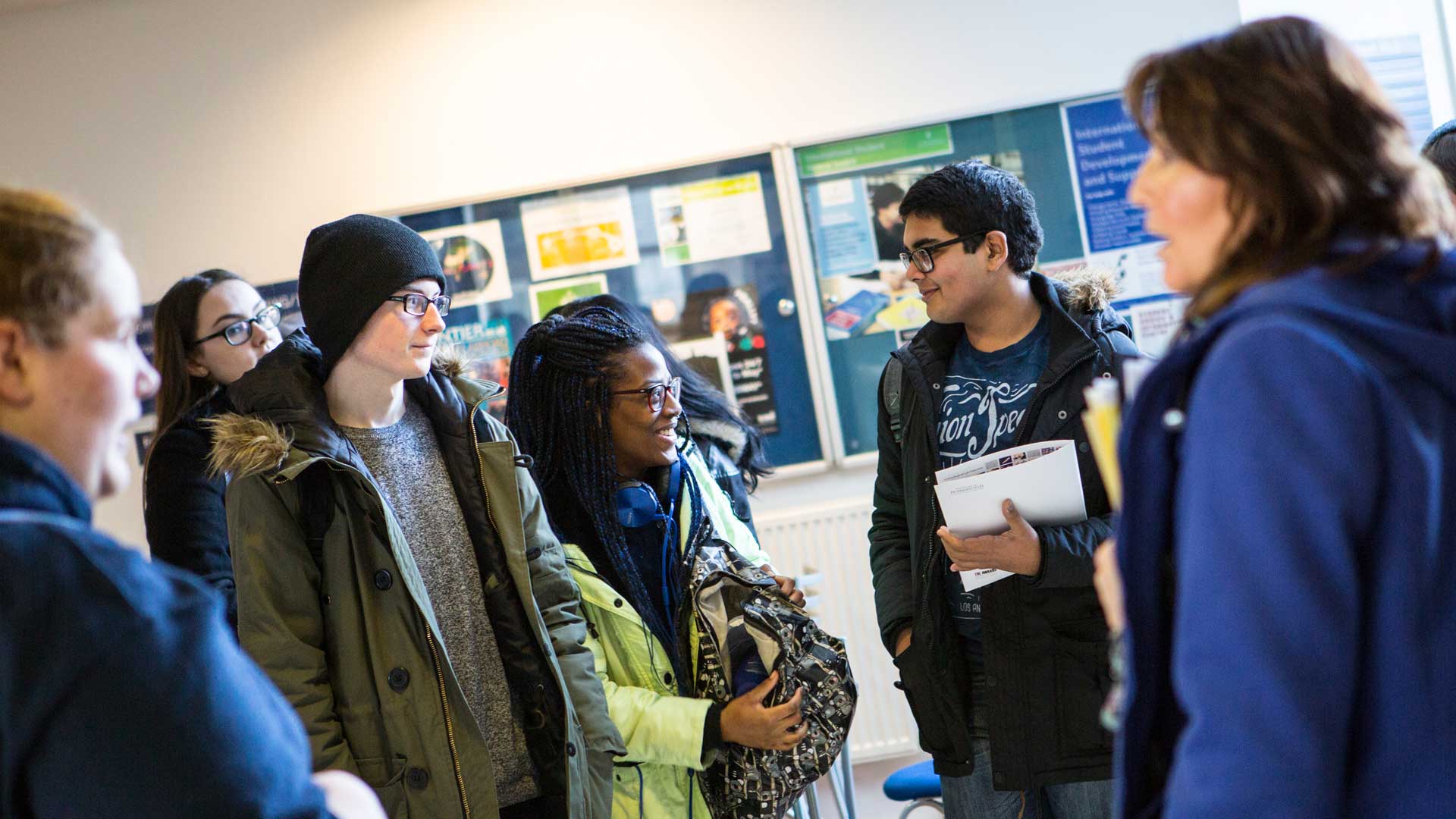 A group of school students standing around listening to their teacher while on a taster day.
