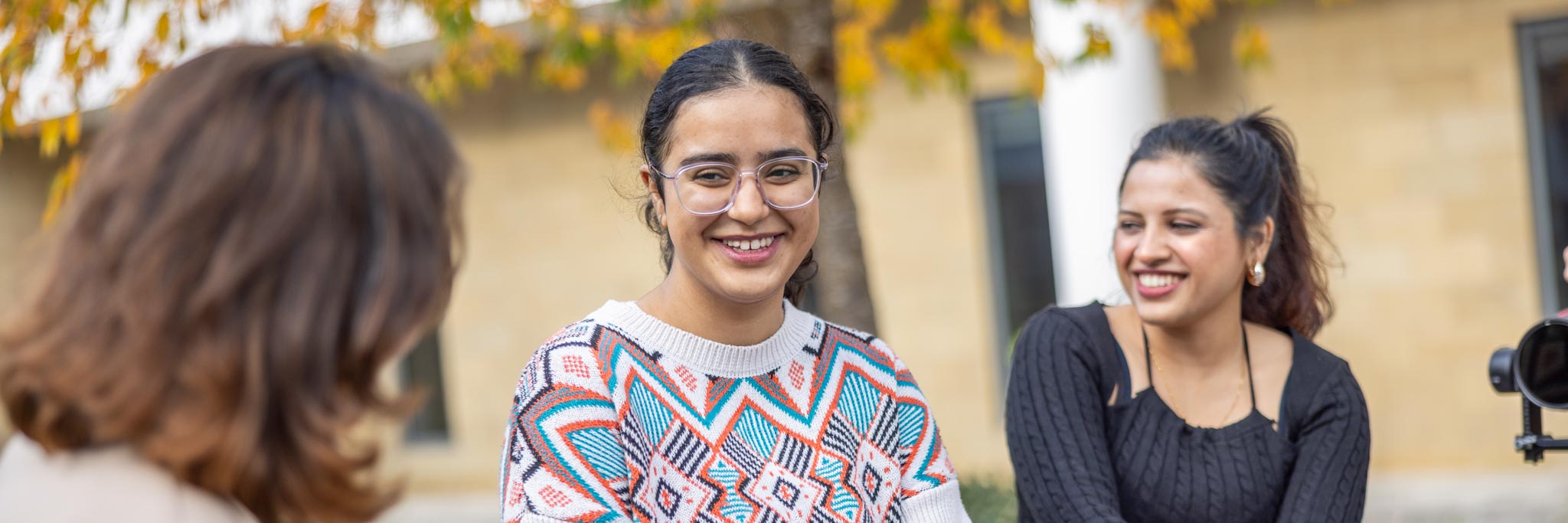 Students smiling and talking with staff member outside