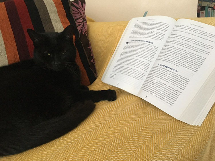 Siobhan's cat sat on a bed next to her open textbook.