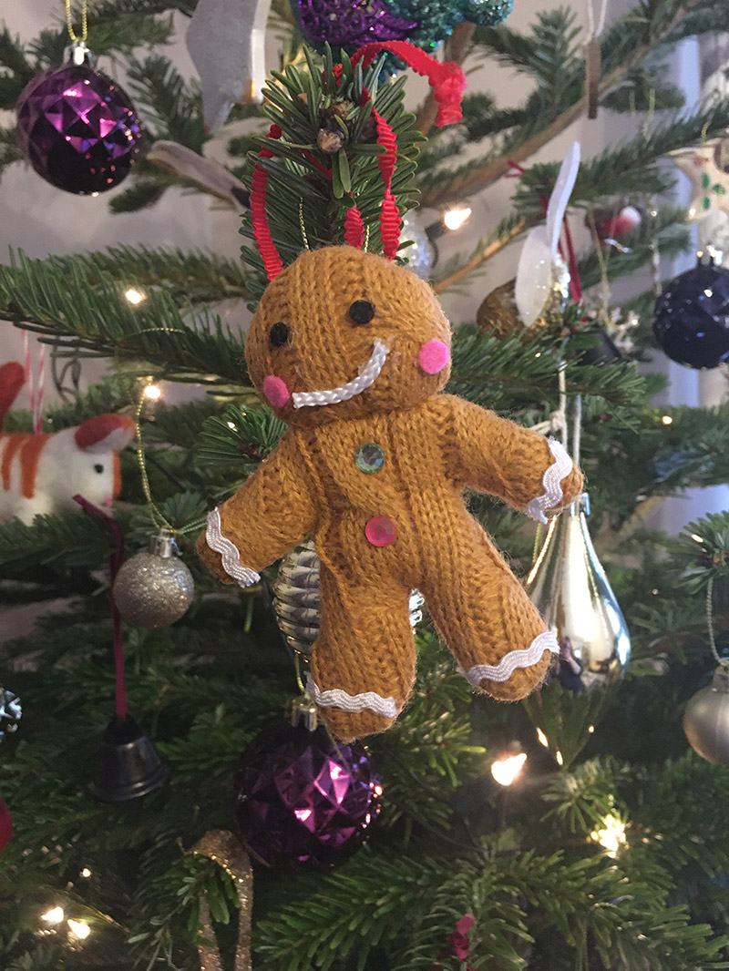 A knitted gingerbread decoration hanging on a Christmas tree.